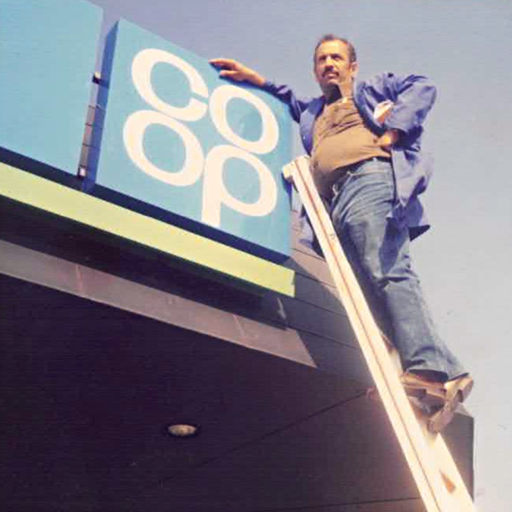 Der Firmengründer Ilyas Özer auf einer Leiter stehend an einem Eingengsschild der früheren Firma COOP