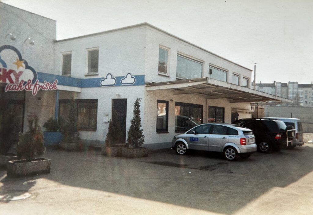 Die frühere Filiale der einstigen Supermarkt-Kette Sky Ende der 1990er Jahre. Vor dem Markt steht ein Silberner Kombi, bedruckt mit dem Özer Logo.